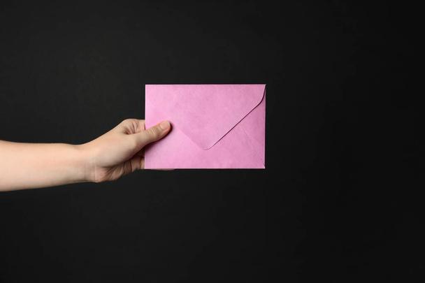 Woman holding pink paper envelope on black background, closeup - Foto, Imagem