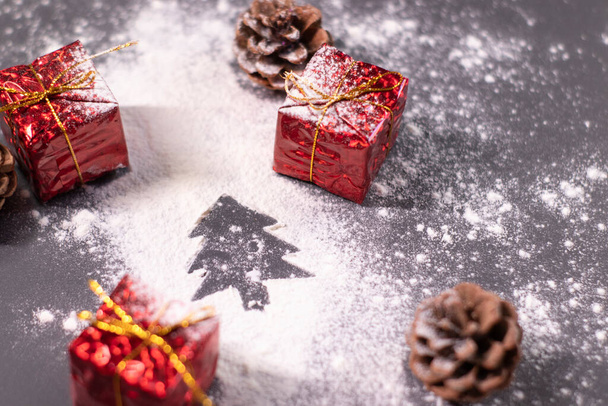 Dekoracje świąteczne, prezenty i szyszki sosnowe w śniegu i sylwetka choinki. Boże Narodzenie. Płaskie zdjęcie - Zdjęcie, obraz