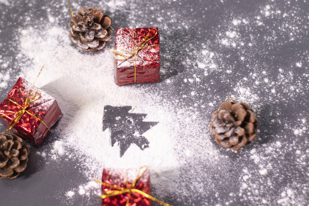 Weihnachtsschmuck, Geschenke und Tannenzapfen im Schnee und die Silhouette eines Weihnachtsbaums. Weihnachtsstimmung. Flaches Foto - Foto, Bild