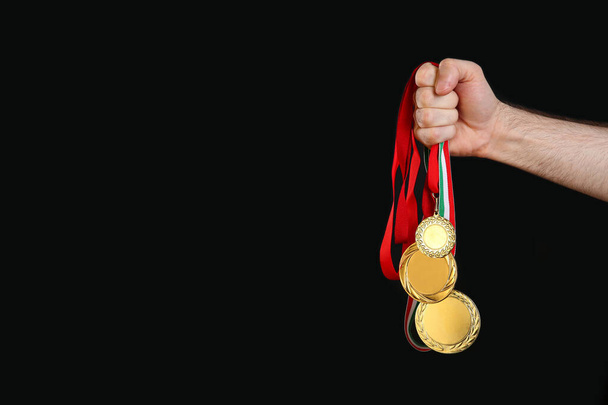 Man holding golden medals on black background, closeup. Space for design - Foto, afbeelding