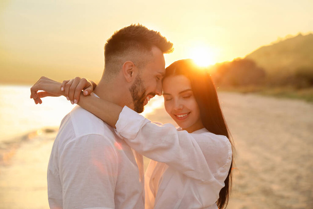 Happy young couple on beach at sunset - Foto, afbeelding