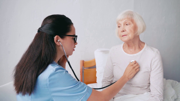 брюнетка медсестра вивчає літню жінку зі стетоскопом
 - Кадри, відео