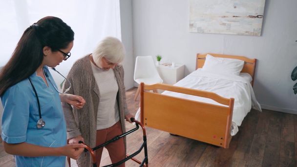ηλικιωμένη γυναίκα που βαδίζει με περιπατητές κοντά σε νοσοκόμοι - Πλάνα, βίντεο