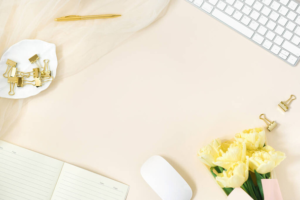 Moderner Home-Office-Schreibtisch, Arbeitsbereich mit Kopierraum, ein Strauß gelber Tulpen auf beigem Hintergrund. Lay Flach, das Layout von oben. Hintergrund für eine freiberufliche Frau oder Bloggerin - Foto, Bild