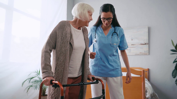 mulher idosa pisando com caminhantes perto de enfermeira geriátrica - Filmagem, Vídeo