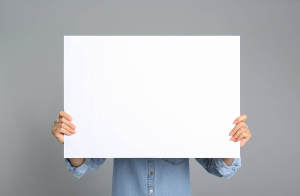 Woman holding white blank poster on grey background, closeup. Mockup for design - Fotó, kép