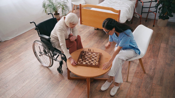 vista de ángulo alto de la mujer en silla de ruedas jugando ajedrez con el médico - Metraje, vídeo