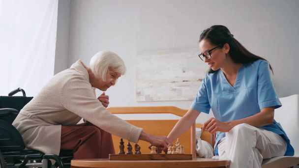 visão lateral da mulher idosa jogando xadrez com enfermeira - Filmagem, Vídeo