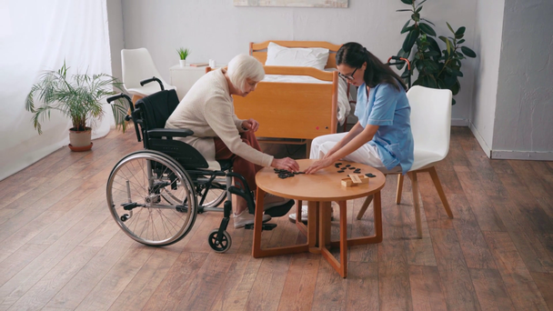 Tekerlekli sandalyedeki yaşlı kadın ve tavla oynayan yaşlı hemşire.  - Video, Çekim