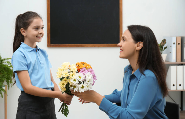 Schoolgirl congratulating her pedagogue with bouquet in classroom. Teacher's day - 写真・画像