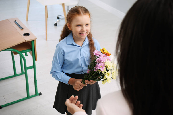 Schoolgirl with bouquet congratulating her pedagogue in classroom. Teacher's day - 写真・画像