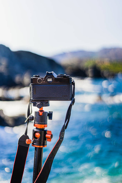 Câmera reflexa preta (analógica) sem marca plantada em um tripé, tirando fotos da paisagem marinha em um dia ensolarado. - Foto, Imagem