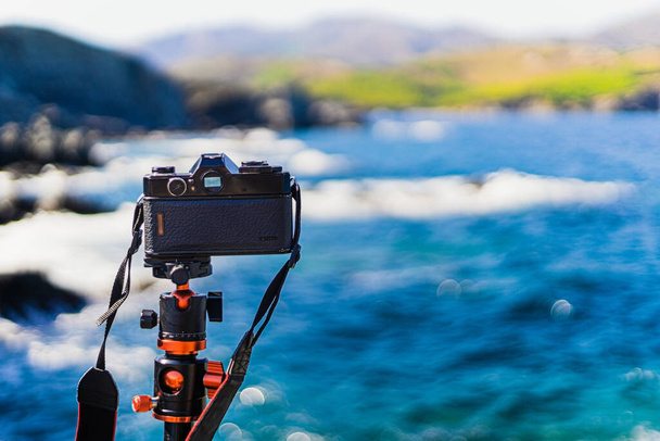 Schwarze (analoge) Spiegelreflexkamera ohne Markennamen auf einem Stativ, die an einem sonnigen Tag die Meereslandschaft fotografiert. - Foto, Bild