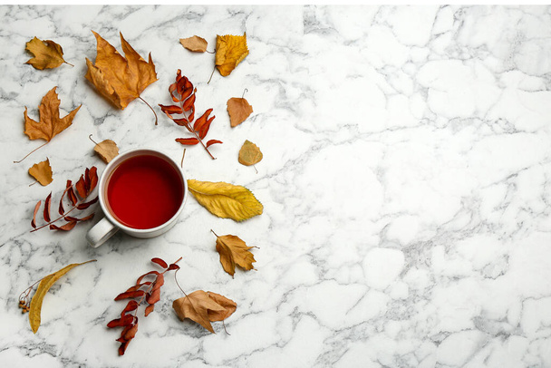 Flat lay composition with cup of hot drink and autumn leaves on white marble background, space for text. Cozy atmosphere - Foto, Imagem
