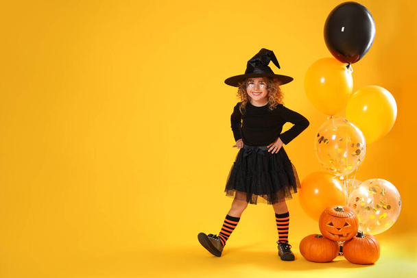 Cute little girl with pumpkins and balloons wearing Halloween costume on yellow background. Space for text - Foto, Imagem