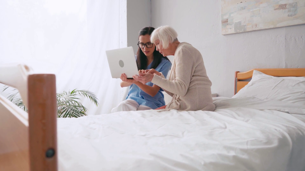 Yaşlı kadın, hemşireyle birlikte dizüstü bilgisayar kullanırken parmağı ile işaret ediyor. - Video, Çekim