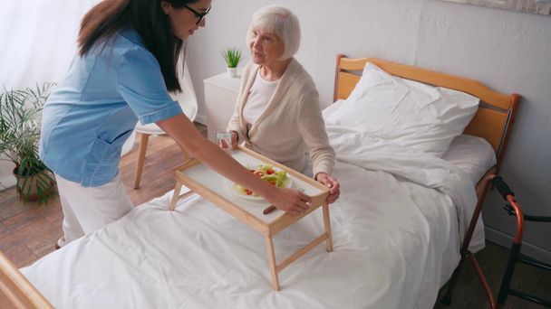 Idős betegeknek tálcát és reggelit szállító idős ápolónő - Felvétel, videó