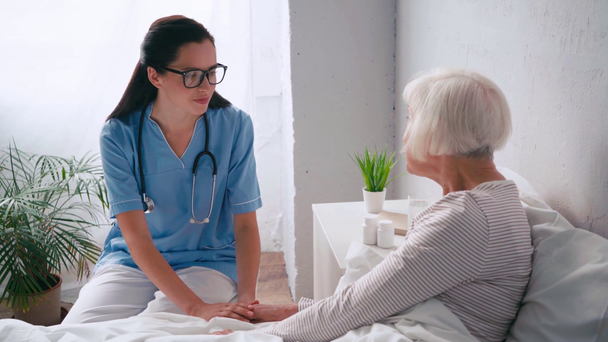 Genç, pozitif yaşlı bir doktor hastanede yaşlı bir kadınla konuşuyor. - Video, Çekim