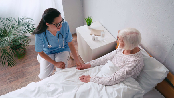 mladá geriatrička a starší žena držící se za ruce a mluvící v nemocnici - Záběry, video