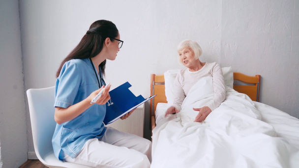 Junge Altenpflegerin spricht mit älterer Patientin und schreibt auf Klemmbrett - Filmmaterial, Video