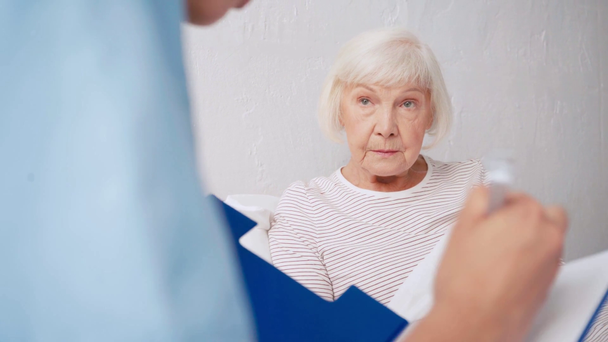 医師がクリップボードに書き込み背景がぼやけている年老いた女性と話すと - 映像、動画