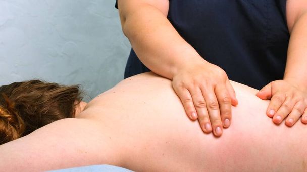 Θεραπευτικό μασάζ στην πλάτη. Θεραπευτής μασάζ κάνει μασάζ σε μια γυναίκα. Έννοια φροντίδας σώματος - Φωτογραφία, εικόνα