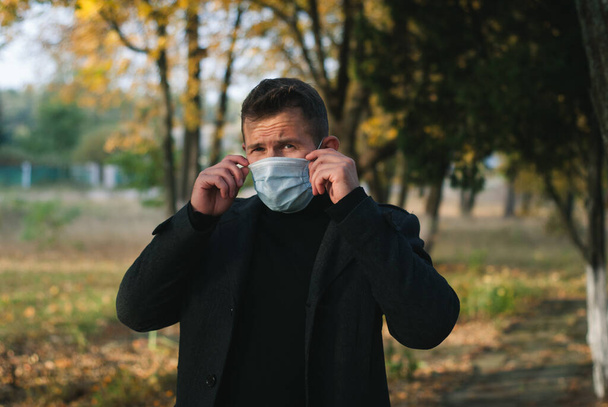 Un homme en manteau sur le fond d'un parc d'automne ajuste un masque médical - Photo, image