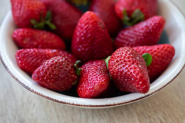 Close-up on a bowl with strawberries on a wooden table. - Photo, Image
