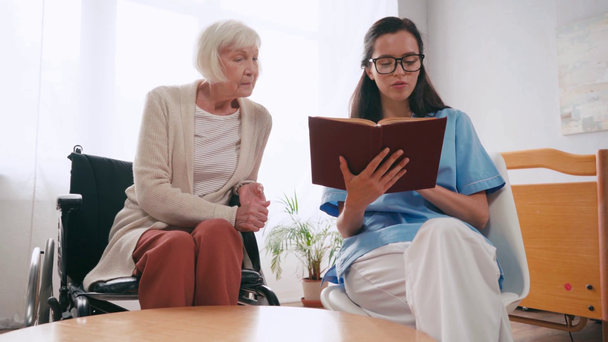 senior femme parler tandis que jeune infirmière lecture livre - Séquence, vidéo
