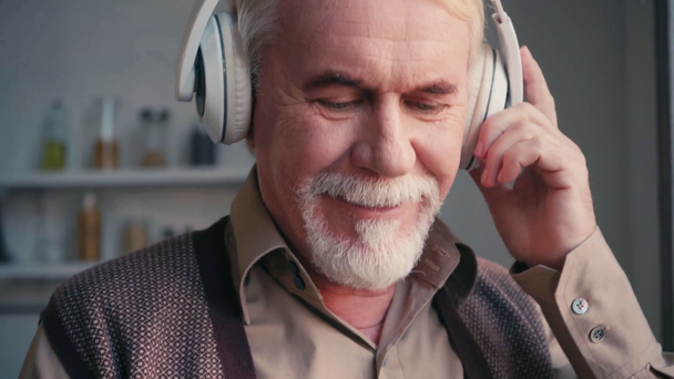 Portrait of positive pensioner in headphones listening to music at home - Footage, Video