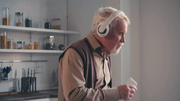 Ευτυχισμένος συνταξιούχος με ακουστικά και smartphone που χορεύει στο σπίτι - Πλάνα, βίντεο