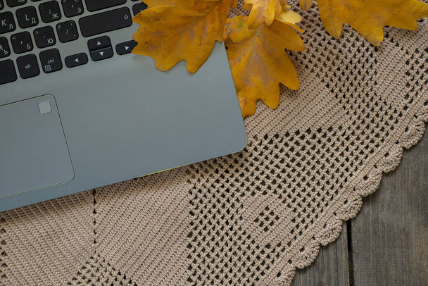 portátil gris se encuentra en una servilleta de encaje marrón en una mesa de madera y una rama de roble amarillo otoño, portátil en la mesa, el estado de ánimo de otoño - Foto, Imagen