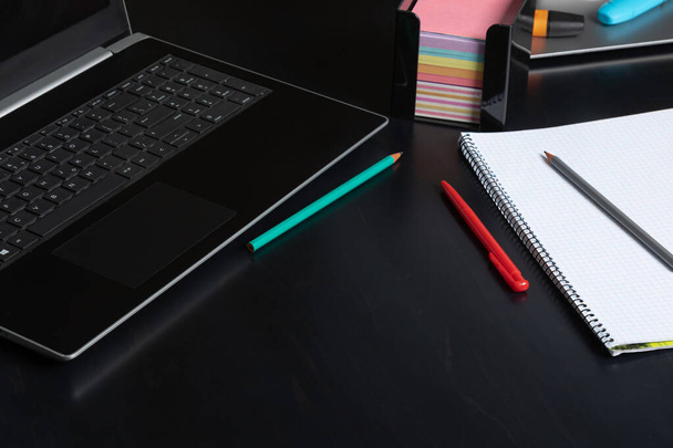 open laptop en blanco notitieblok met potloden op donkere tafel - Foto, afbeelding
