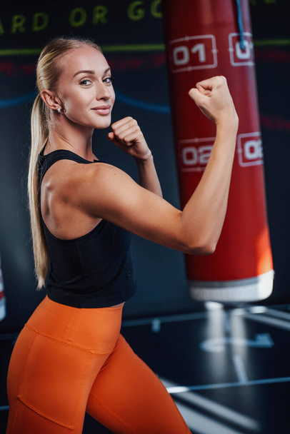 Позитивная женщина позирует с боксерскими грушами на заднем плане - Фото, изображение