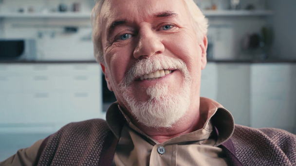 Portret szczęśliwego emeryta patrzącego na kamerę z zamazaną kuchnią na tle - Materiał filmowy, wideo