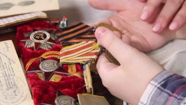 Vrouwen en kinderhanden sorteren medailles uit de Tweede Wereldoorlog. - Video