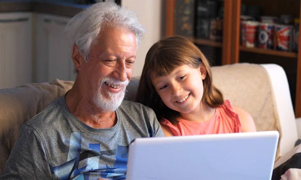Büyükbaba ve torun bilgisayara bir video görüşmesi yaparak selamlaşıyorlar. - Fotoğraf, Görsel