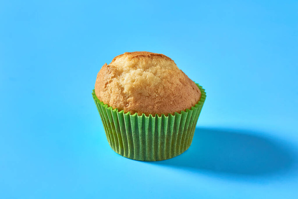 One fluffy muffin in green paper mold on blue background - Fotoğraf, Görsel