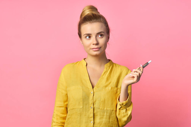 Young beautiful woman with a vape on a pink wall background. - Photo, Image