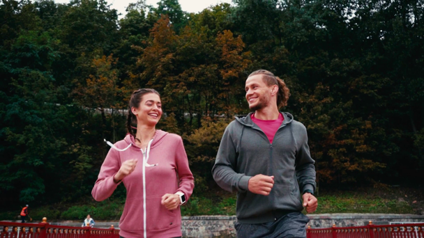 Усміхнена пара бігунів біжить по мосту з парком на фоні, повільний рух
 - Кадри, відео