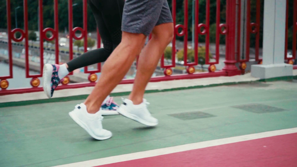 Vista recortada de la pareja en zapatillas de deporte corriendo a lo largo de la trayectoria en el puente - Metraje, vídeo