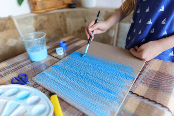 het meisje tekent blauw gouache karton, maakt een achtergrond, zit in de huiskeuken - Foto, afbeelding
