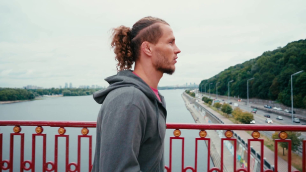 Vista laterale dell'uomo barbuto che corre sul ponte con la città sullo sfondo, rallentatore - Filmati, video