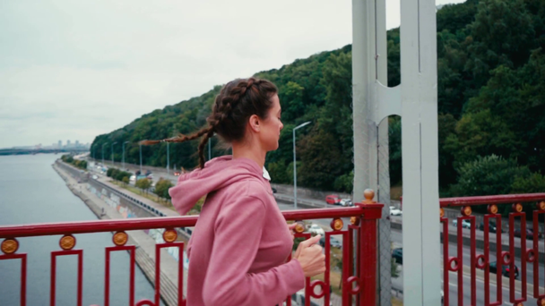 Femme brune courant sur le pont avec la ville en arrière-plan, ralenti - Séquence, vidéo