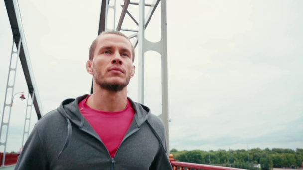 Εστιασμένος άνθρωπος σε αθλητικά που τρέχει σε γέφυρα με συννεφιασμένο ουρανό στο παρασκήνιο - Πλάνα, βίντεο