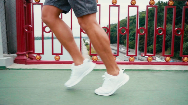 Περικοπή άποψη του ανθρώπου σε sneakers τρέχει στη γέφυρα με την πόλη στο παρασκήνιο - Πλάνα, βίντεο