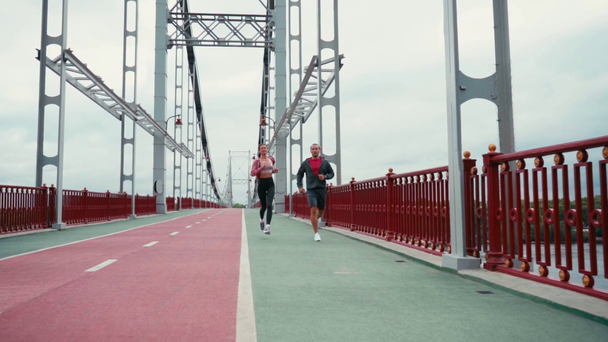 Pareja de corredores corriendo en puente con cielo nublado sobre fondo, cámara lenta - Metraje, vídeo