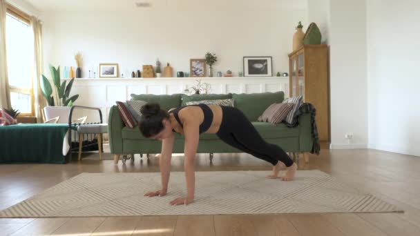 Girl is stretching on carpet in living room. Sporty woman is doing yoga poses in dynamic, down face dog and upward facing dog poses. Sport and home fitness. Training, workout and wellness concept. - Footage, Video