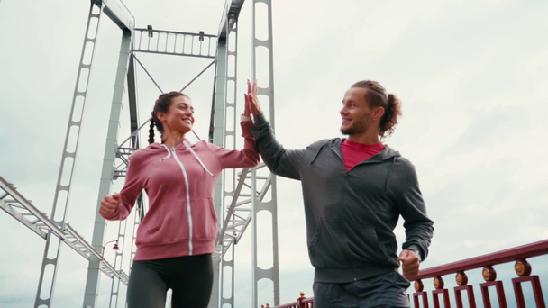 Köprüde koşan ve beşlik çakan mutlu koşucuların düşük açılı görüntüsü - Video, Çekim