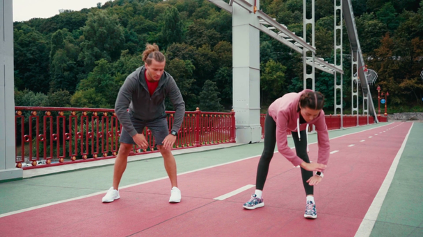 Férfi és nő a sportruházatban nyújtózik a hídon a természettel a háttérben - Felvétel, videó